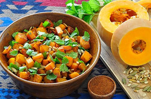 butternut squash cut in half with seeds sprinkled around next to a bowl of cooked butternut squash dish